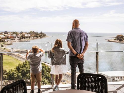 a man and two children standing on a balcony looking at the ocean at Novotel Devonport in Devonport