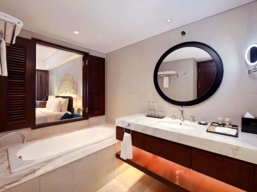a bathroom with a tub and a sink and a mirror at Grand Mercure Bali Seminyak in Seminyak