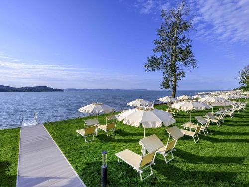 a row of chairs and umbrellas next to the water at Mövenpick Balaland Resort Lake Balaton in Szántód