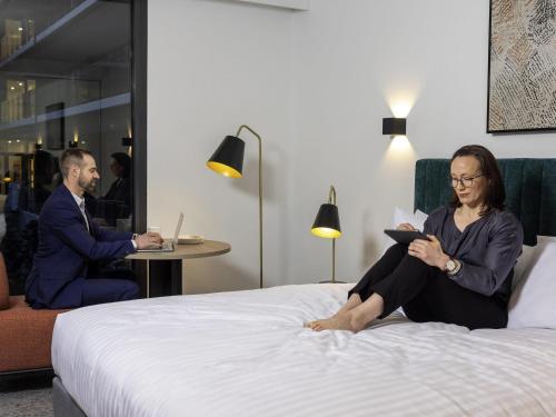 a man and a woman sitting on a bed at The Sebel Canberra Campbell in Canberra