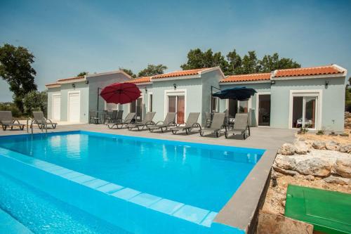 a pool with chairs and umbrellas next to a house at Apartment Maxi in Karavadhos