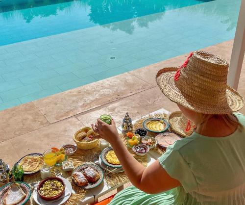 a woman in a straw hat sitting at a table with food at Villa Jardins D'Isa in Marrakech