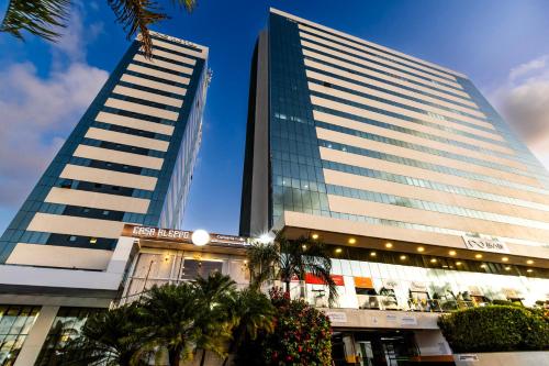 two tall buildings with palm trees in front of them at Mais Hotel Aeroporto Salvador in Lauro de Freitas