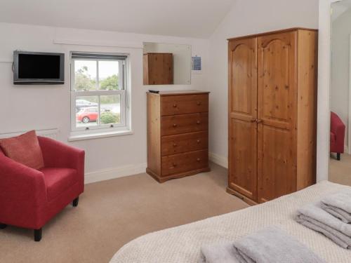 a bedroom with a bed and a dresser and a red chair at Garth Cottage in Haverfordwest