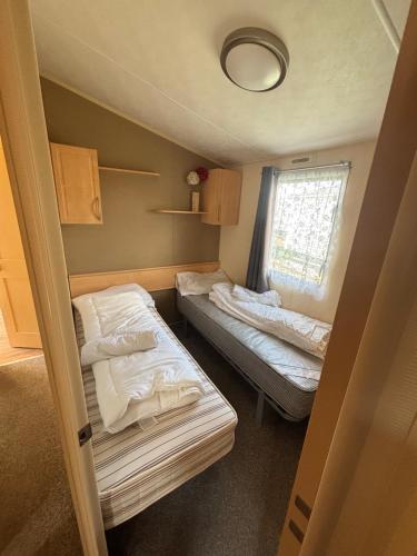 a small room with two beds and a window at Singh&Leite Family caravan for 6 people in Saint Osyth