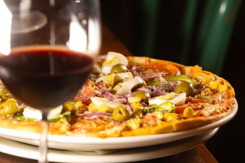 a pizza on a plate next to a glass of wine at Mais Hotel Aeroporto Salvador in Lauro de Freitas
