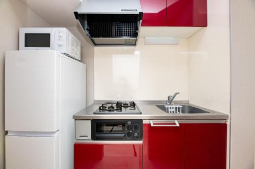 a small kitchen with red cabinets and a white refrigerator at SPAZIO 6 Hakata Station in Fukuoka