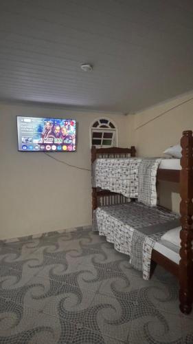 a bedroom with two beds and a tv on the wall at Pousada Hostel Shalom in Rio das Ostras