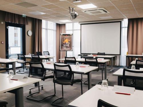 a classroom with tables and chairs and a white screen at Ibis Rouen Centre Rive Gauche Mermoz in Rouen