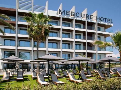 a group of lounge chairs and umbrellas in front of a hotel at Mercure Larnaca Beach Resort in Larnaka