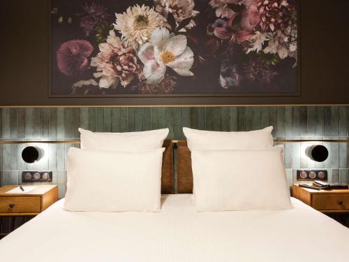 a bed with white pillows and a painting on the wall at Hotel Les Capitouls Toulouse Centre - Handwritten Collection in Toulouse
