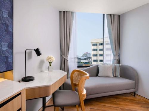 a room with a desk and a couch with a window at Novotel Rayong Star Convention Centre in Rayong