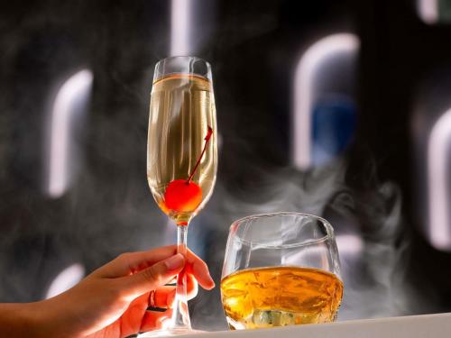 a person holding a wine glass with a red object in it at Novotel Rayong Star Convention Centre in Rayong