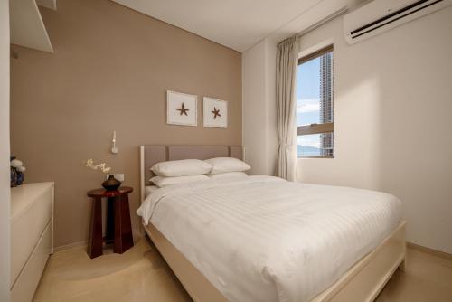 a white bedroom with a bed and a window at Amber Bay Hotel & Suites Da Nang in Danang