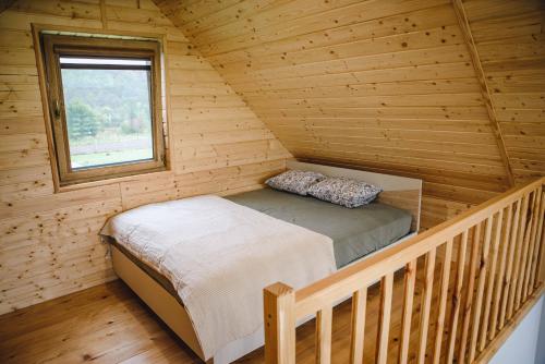 a bed in a wooden cabin with a window at Domki nad Wiarem in Huwniki