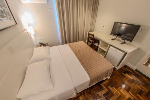 a bedroom with a bed and a desk with a television at Hotel Centro Europeu in Curitiba