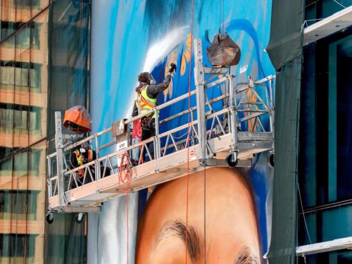 a group of workers painting a large advertisement on a building at The Adnate Perth - Art Series in Perth
