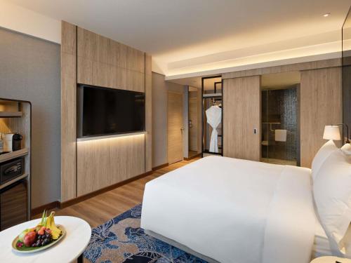 a bedroom with a large white bed and a table with a plate of fruit at Mövenpick Hotel Jakarta City Centre in Jakarta