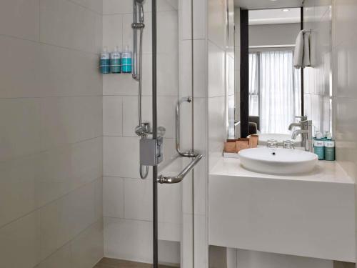 a white bathroom with a sink and a shower at Novotel Living Saigon South in Ho Chi Minh City