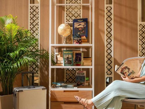 a woman sitting in a chair reading a book at Andaman Beach Hotel Phuket - Handwritten Collection in Patong Beach