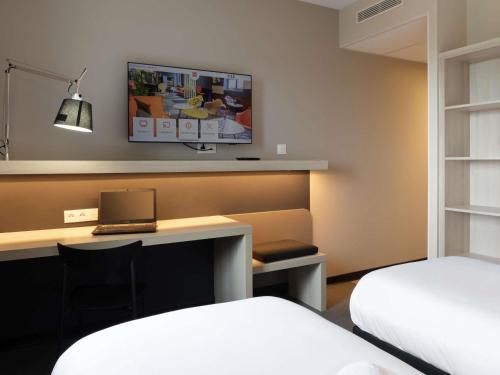 a hotel room with a desk with a laptop and a tv at ibis Douai Dechy in Dechy