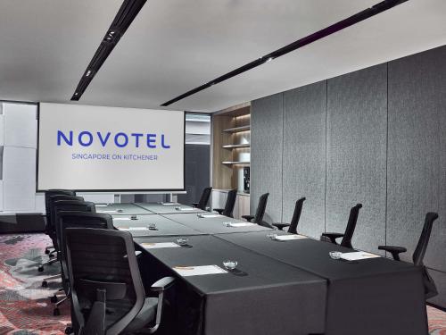 a conference room with a long table with chairs and a screen at Novotel Singapore on Kitchener in Singapore