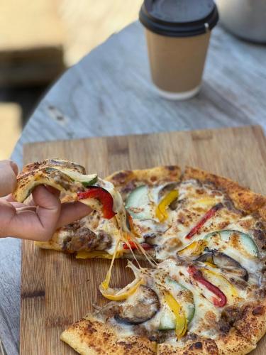 a person holding a slice of pizza on a cutting board at 'Yamaneko Hotel 'Saunas, Serenity & Feline Friends in Miyoshi