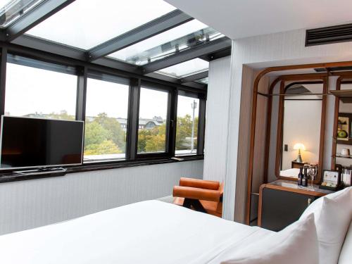 a bedroom with a bed and a tv and windows at MUZE Hotel Dusseldorf - Handwritten Collection in Düsseldorf