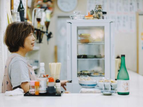 a woman sitting at a counter in a kitchen at SEKAI HOTEL Deep Osaka Experience in Osaka