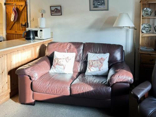 a brown leather couch with two white pillows on it at Blacksmiths Cottage in Gillamoor