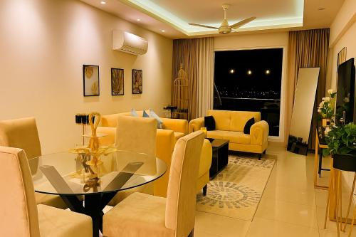 a living room with a glass table and yellow chairs at Gold Crest Executive Hotel Apartments City View DHA Lahore in Lahore