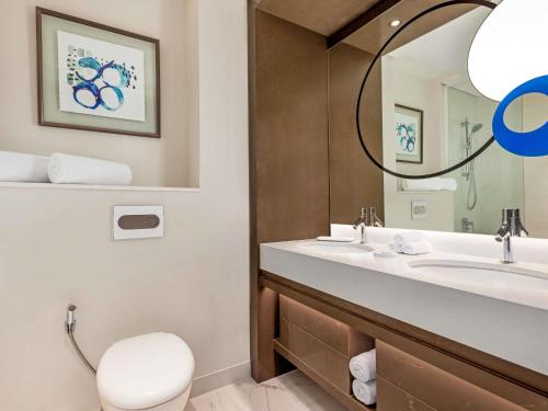 a bathroom with a sink and a toilet and a mirror at Novotel Dubai Gold District in Dubai