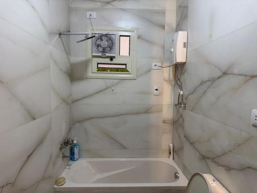 ein weißes Badezimmer mit Badewanne und Fenster in der Unterkunft رويال روف بالتجمع الخامس أمتداد الجامعة الامريكية in New cairo