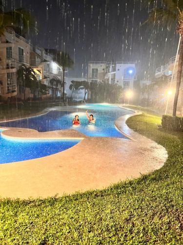 two people swimming in a swimming pool in the rain at Departamento planta baja en la laguna in Acapulco