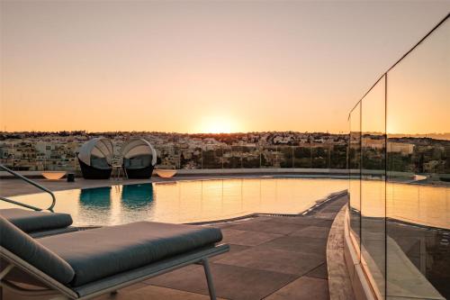 a pool on the roof of a building with the sunset at Hyatt Regency Malta in St Julian's