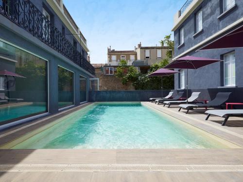 une piscine avec chaises et parasols à côté d'un bâtiment dans l'établissement Kyriad Marseille Blancarde - Timone, à Marseille