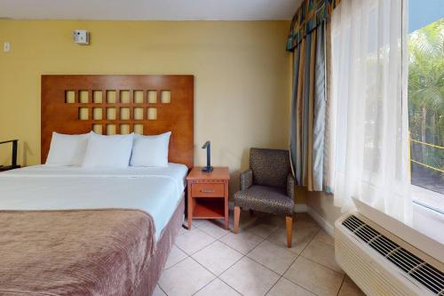 a bedroom with a bed and a chair and a window at Rodeway Inn & Suites Fort Lauderdale Airport & Cruise Port in Fort Lauderdale