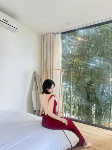 a woman in a red dress sitting on a bed at Dreamy Homestay Tam Đảo in Tam Ðảo