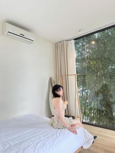 a woman sitting on a bed looking out a window at Dreamy Homestay Tam Đảo in Tam Ðảo