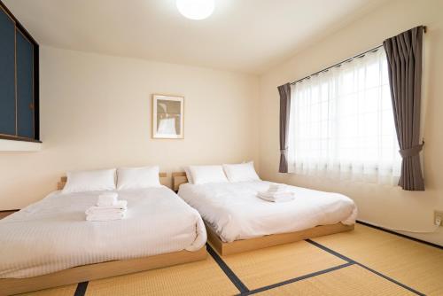 Dos camas en una habitación con ventana. en Tsubaki オーシャンビュー 観光拠点 閑静な住宅街, en Otaru