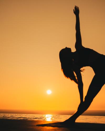a woman doing yoga on the beach at sunset at Magma Resort Santorini, In The Unbound Collection By Hyatt in Vourvoulos