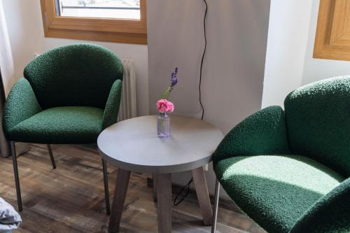 two green chairs and a table with a vase with flowers at BnB Feuille de Vigne in Saint-Léonard