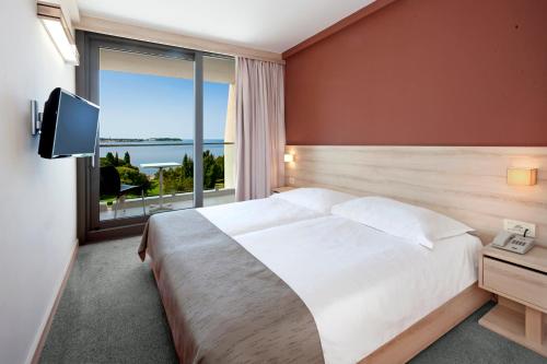 a bedroom with a large bed and a large window at Hotel Materada Plava Laguna in Poreč