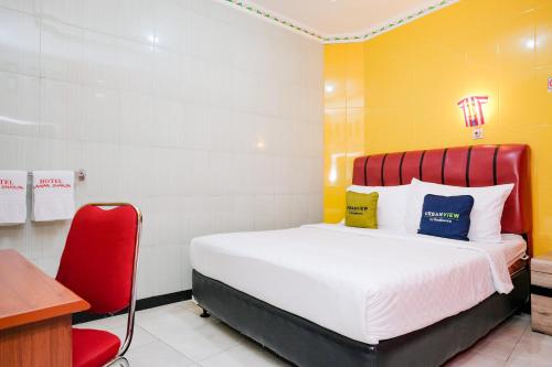 a bedroom with a bed and a red chair at Urbanview Hotel Mawar Sharon near Alun Alun Batu in Batu