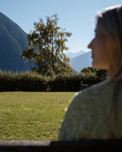 a woman sitting on a bench looking at a field at Farmhotel Moosmair in Campo Tures