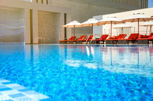 a swimming pool with red chairs and umbrellas at Downtown Rotana in Manama