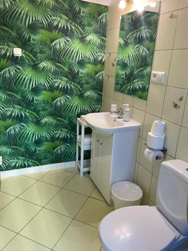 a bathroom with a toilet and a sink with a green leaf wallpaper at Apartamenty Konopnicka in Bydgoszcz