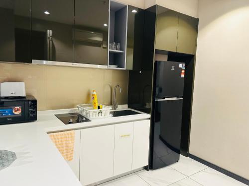 a kitchen with white cabinets and a black refrigerator at KLcc suites astra 8 kia peng in Kuala Lumpur