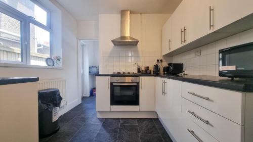 a kitchen with white cabinets and a stove top oven at Cosy bright 4 bed house 11mins from Cardiff centre in Cardiff