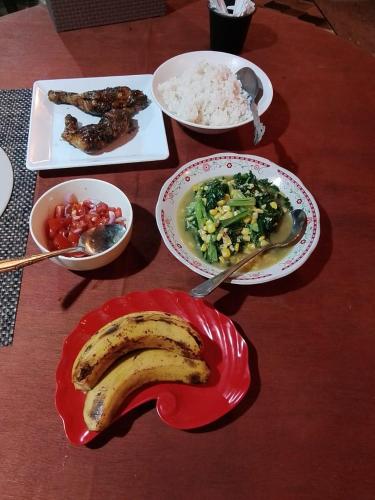 a wooden table with plates of food and a banana at Three Ken Homestay & Cafe in Manado